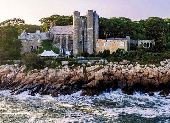 Photograph of the Hammond Castle. A large medieval structure built out of stone. The castle is at the edge of a rocky shoreline by the ocean.