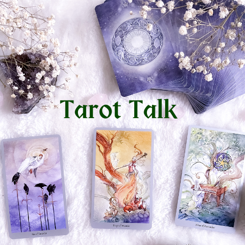 Tarot talk. Tarot cards lying on a table. A stack of cards is fanned out. Three cards are face up. The cards are illustrated with pallets that include a lot of purple. The images include women in flowing white dresses, swans, crows, foxes, trees, and a piano. Also on the table are small white flowers and a white smooth stone.