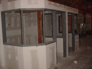 Partially constructed interior office with unfinished drywall and metal framing for windows and doors, located inside a larger building with exposed beams and concrete flooring.