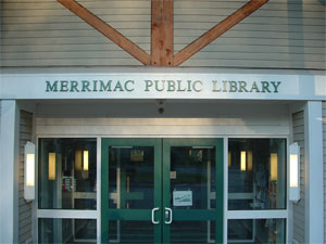 Entrance of Merrimac Public Library with double glass doors and the library name displayed above the entrance in green letters.