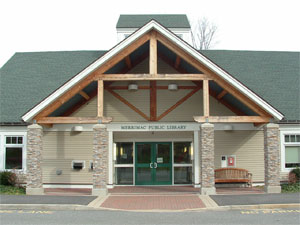 Front view of a public library building with stone columns, wooden beams, a green roof, double glass doors, a bench to the right, and a mailbox to the left of the entrance.